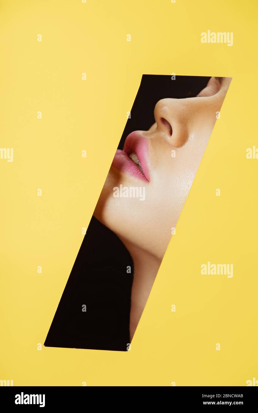Cropped view of female face with pink lips in quadrilateral hole in ...