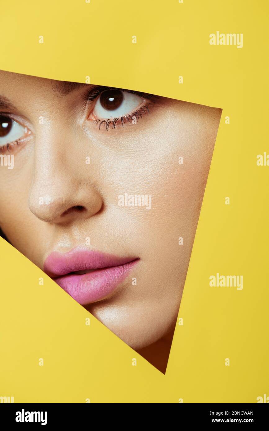 Woman with pink lips looking across triangular hole in yellow paper ...
