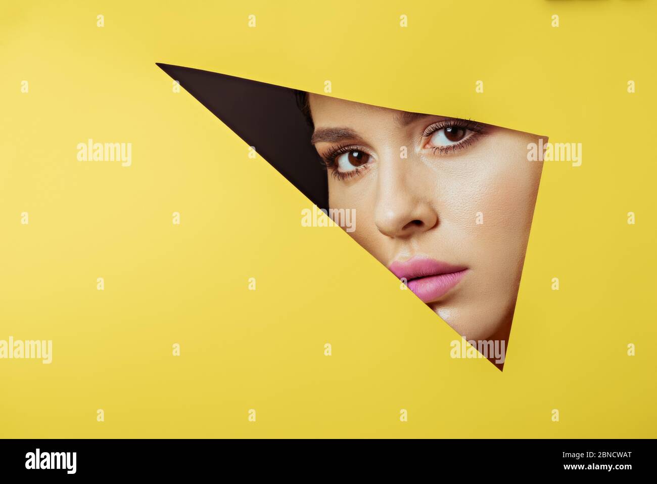 Woman with pink lips looking at camera across triangular hole in yellow ...