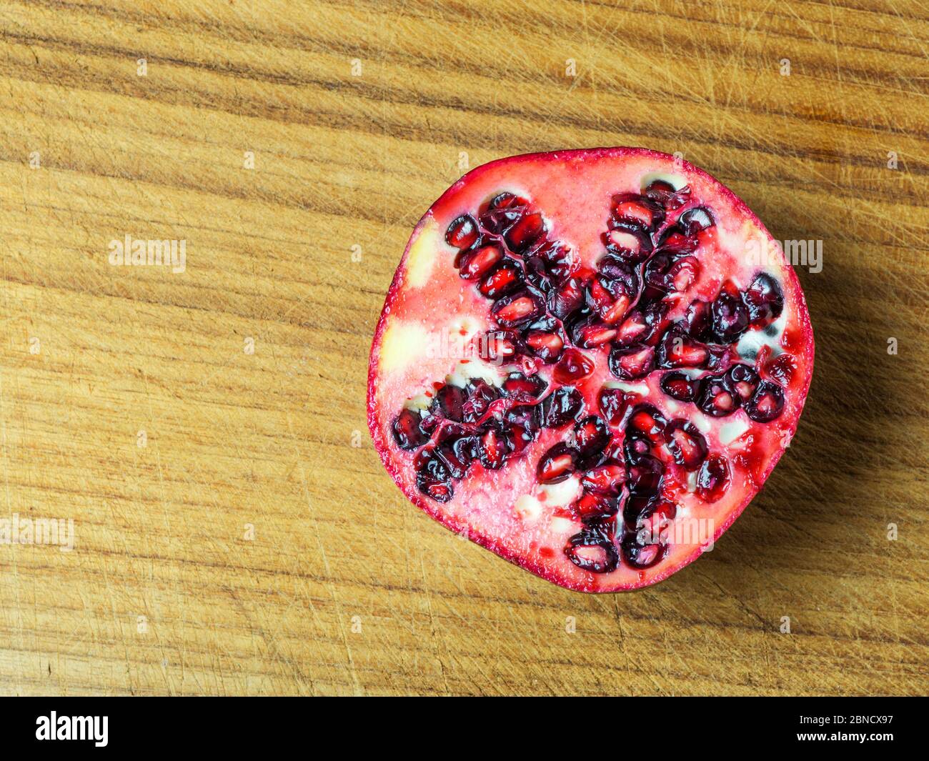 Half a fresh pomegranate on a wooden chopping board with copy space Stock Photo