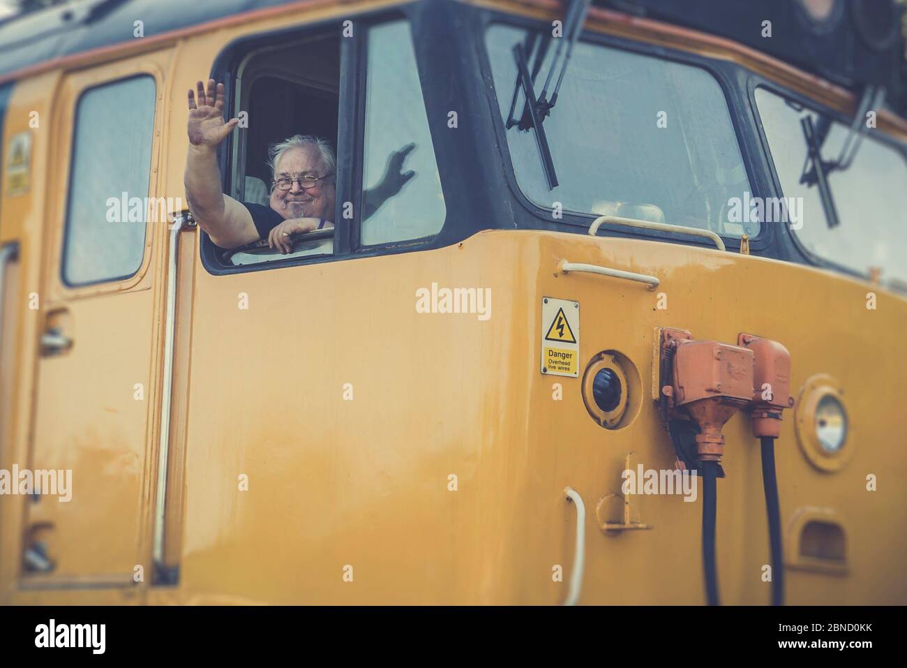 Retro front view close up, British vintage diesel locomotive leaving station, Severn Valley heritage railway, UK. Train driver waving from cab window. Stock Photo