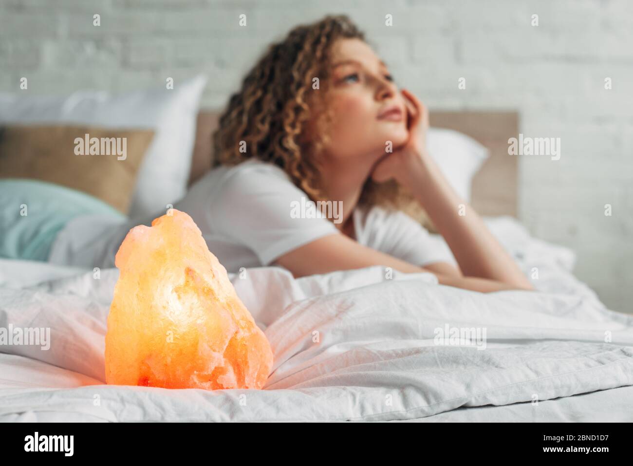 thoughtful girl lying on bed with Himalayan salt lamp, selective focus Stock Photo