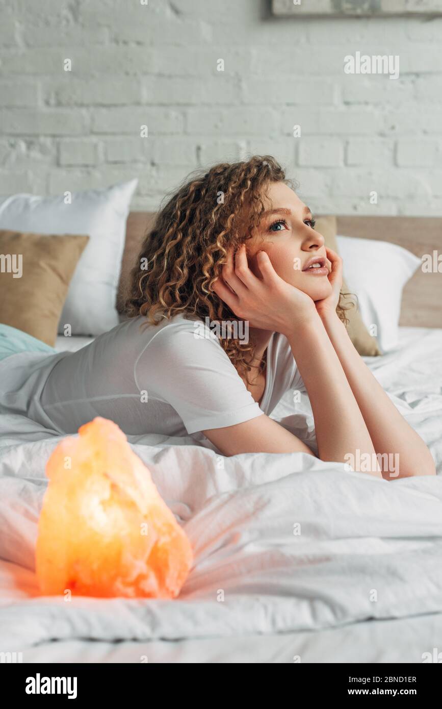 beautiful thoughtful girl lying on bed with Himalayan salt lamp, selective focus Stock Photo