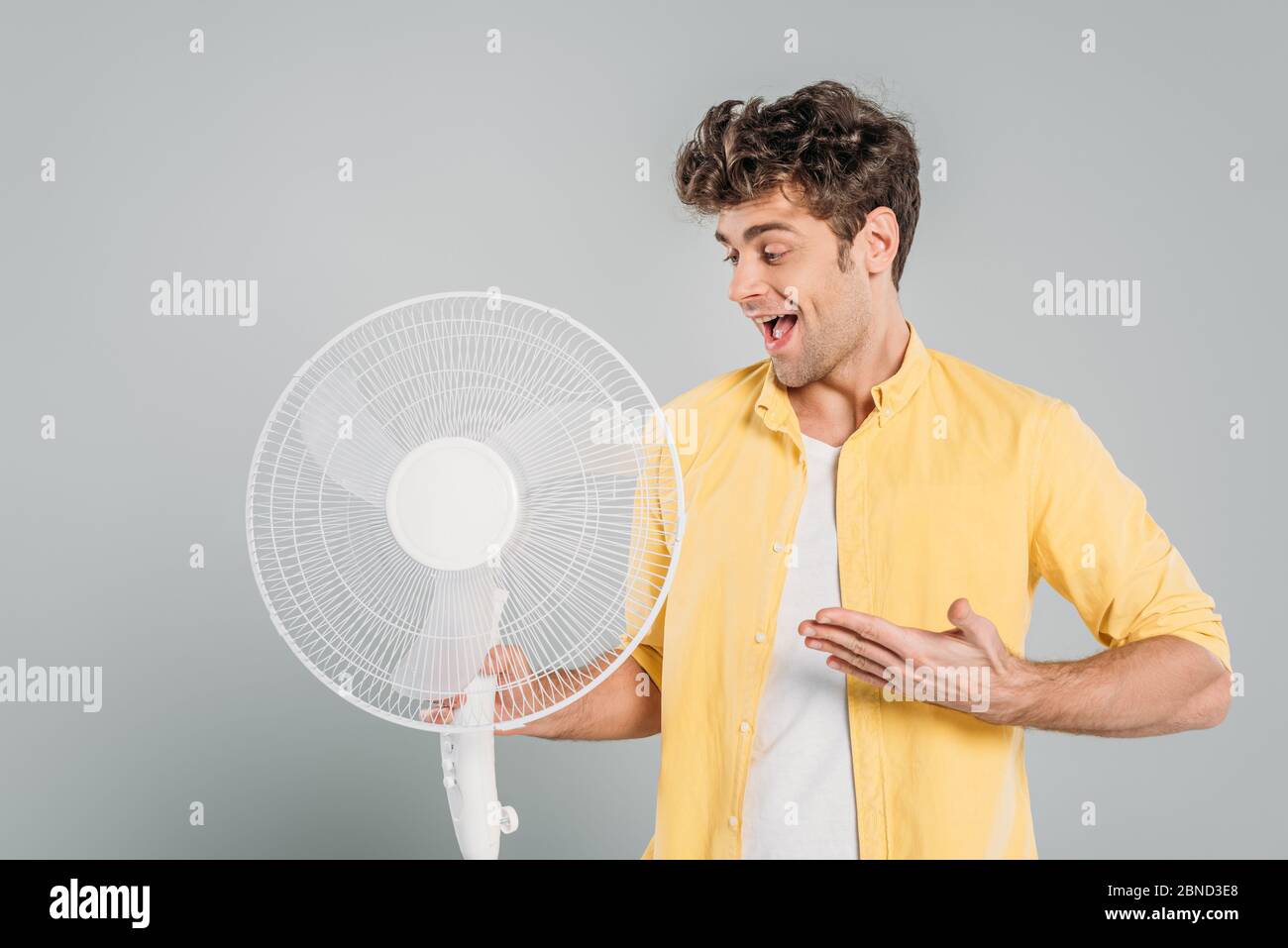 Man with open mouth pointing at electric fan isolated on grey Stock ...