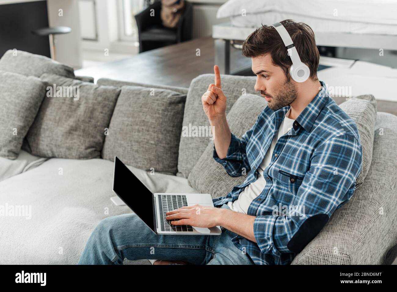 Freelancer in headphones having idea and using laptop on sofa at home ...