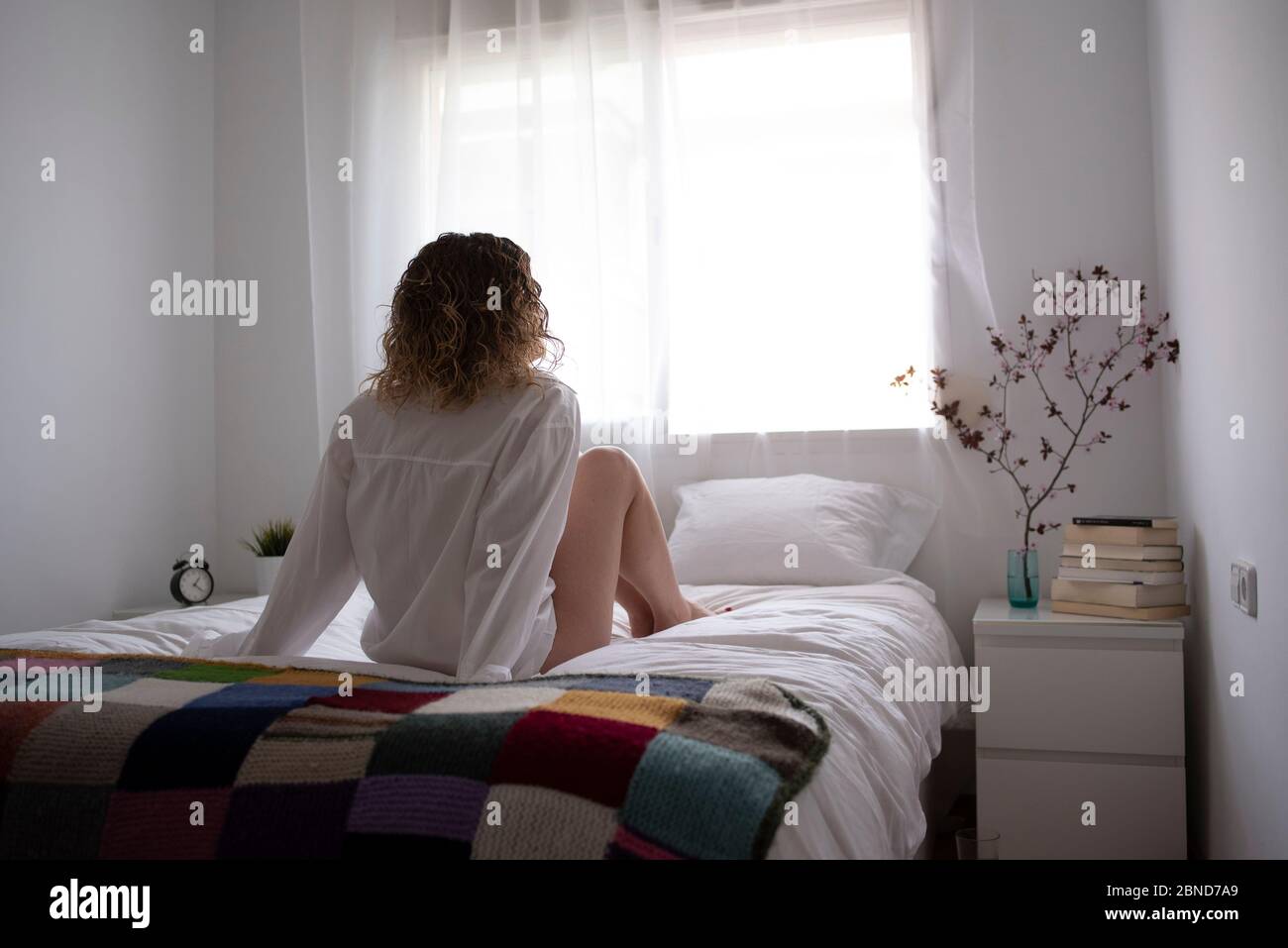 Woman in white shirt sitting back to camera on the bed Stock Photo