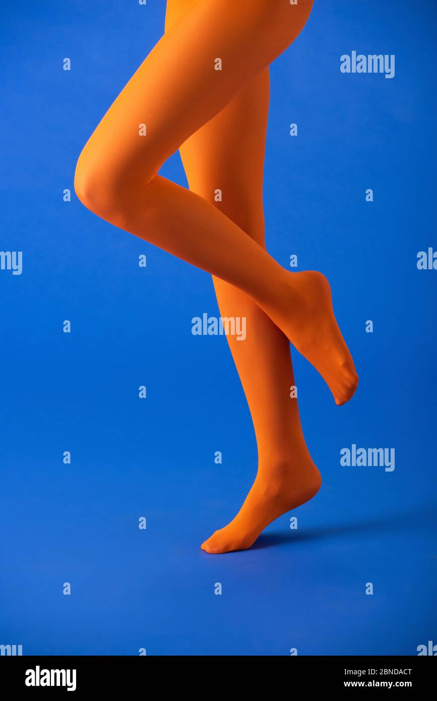 cropped view of woman in bright orange tights posing on blue Stock