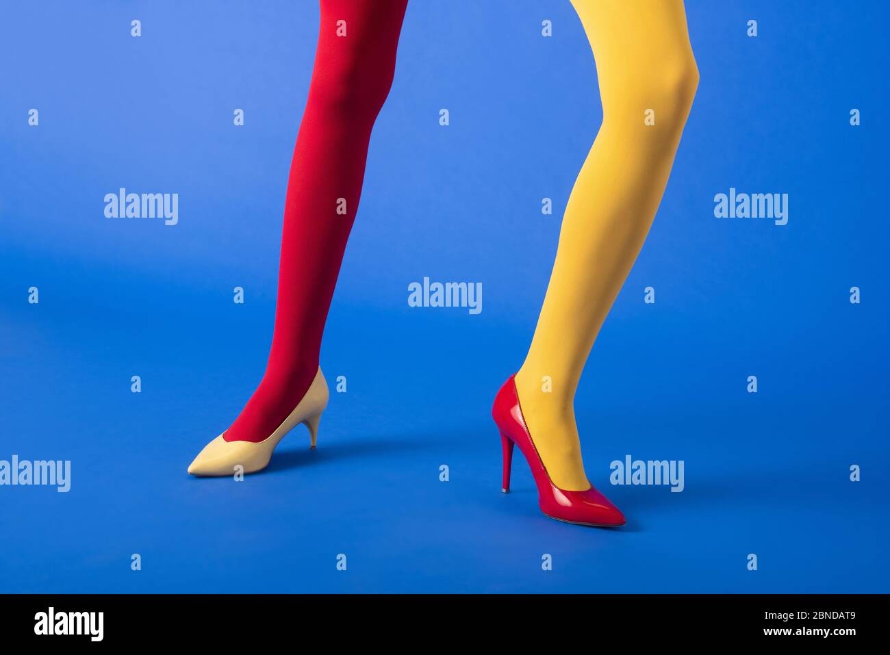 cropped view of woman in yellow and red tights and heels posing on blue ...