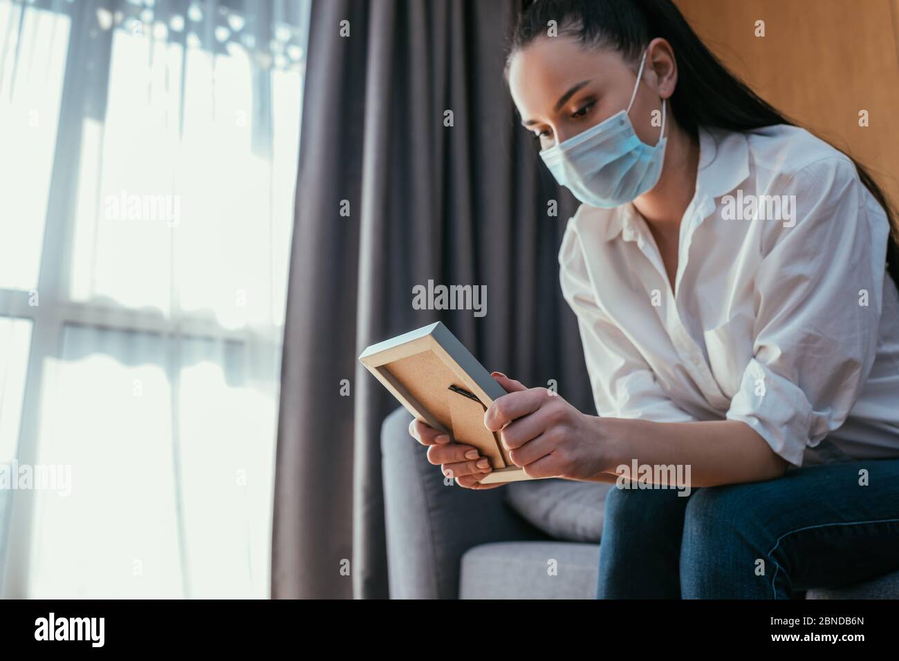 sad young woman in protective mask holding photo of boyfriend while sitting at home Stock Photo