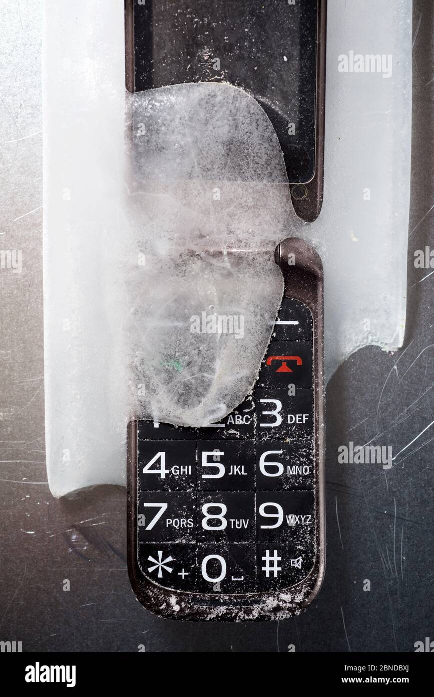 Frozen old mobile phone on a metal table. Stock Photo