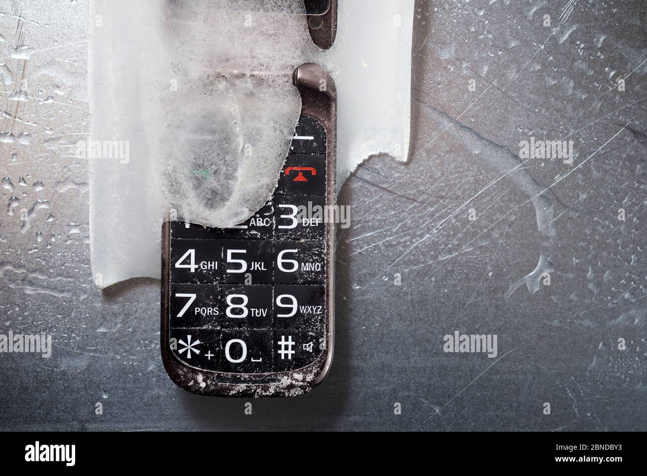 Frozen old mobile phone on a metal table. Stock Photo