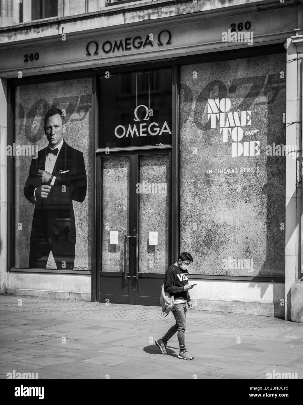 Monochrome image of a person in a face mask by the 'No Time To Die' James Bond sign on a deserted Regent Street in London during the lockdown. Stock Photo