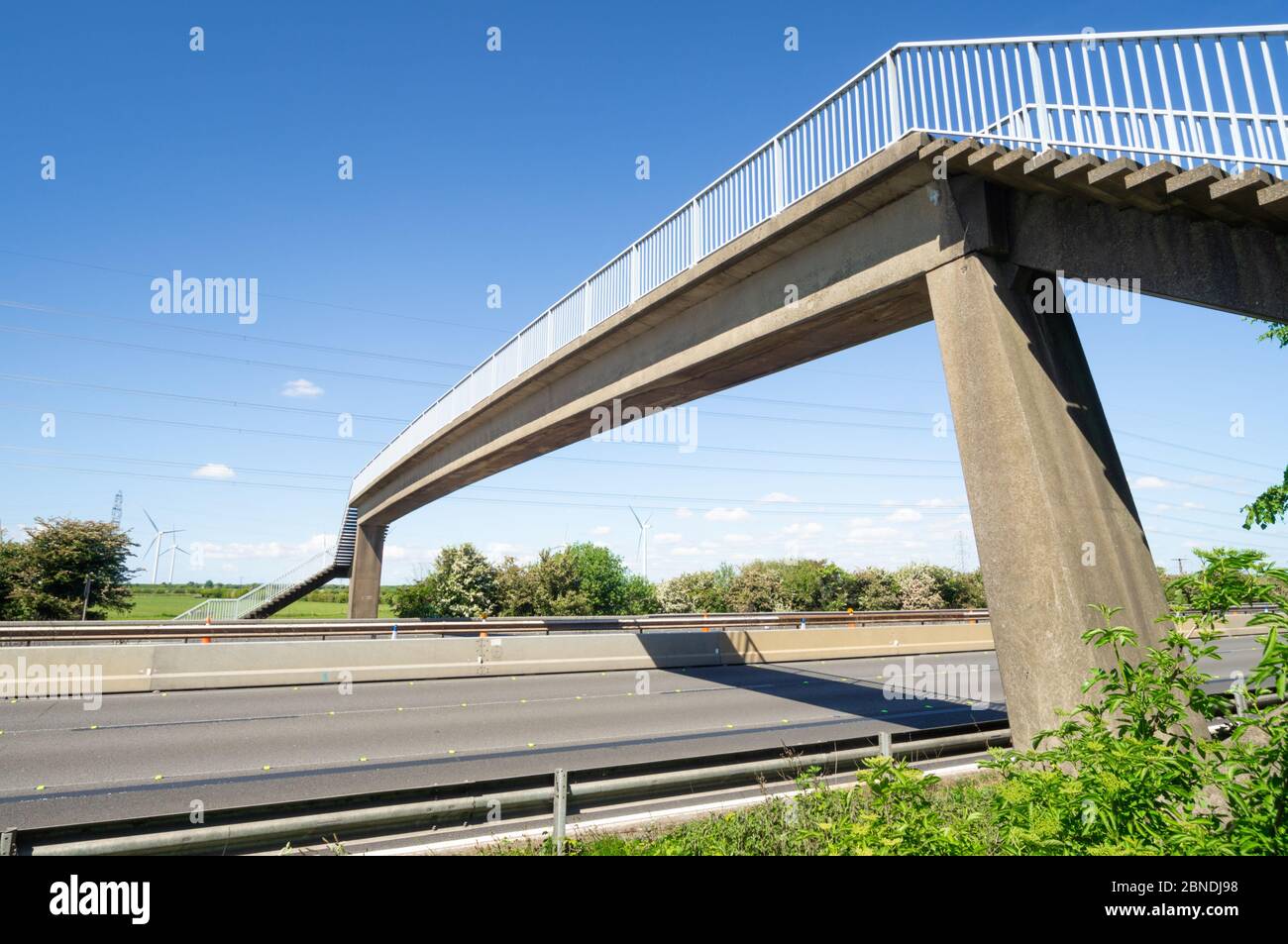 Motorway bridge over the M56 near Frodsham, empty with no traffic and blue sky with wind turbines, Cheshire, England, UK Stock Photo