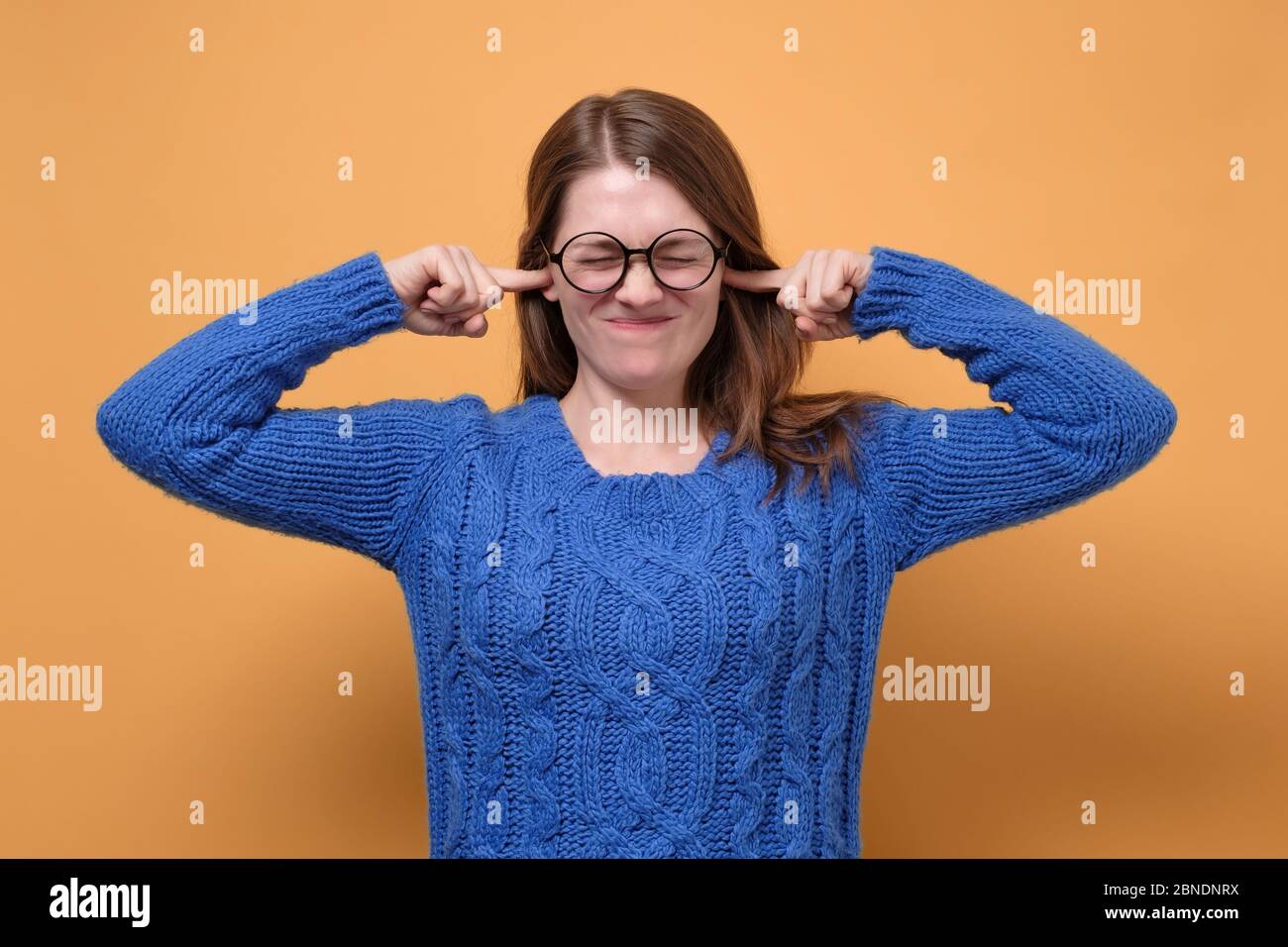 Young female in glasses having discontent look plugging her ears being annoyed with noise wanting silence and calm atmosphere being exhausted Stock Photo