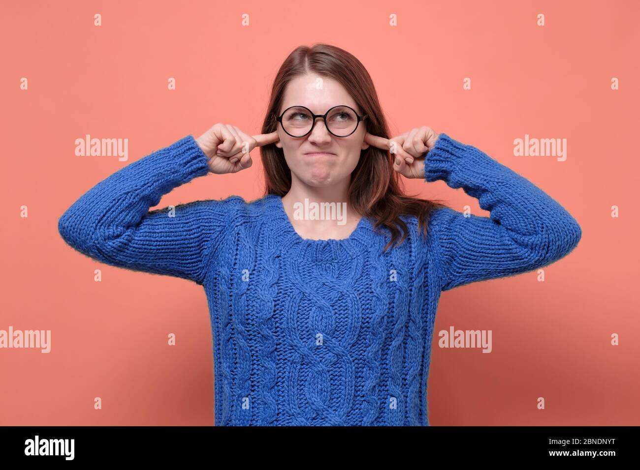 Young female in glasses having discontent look plugging her ears being annoyed with noise wanting silence and calm atmosphere being exhausted Stock Photo