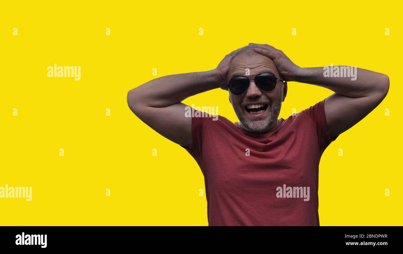The man holds his hands behind his head and screams from despair and disappointment, his eyes are full of horror, his mouth opened. Stock Photo