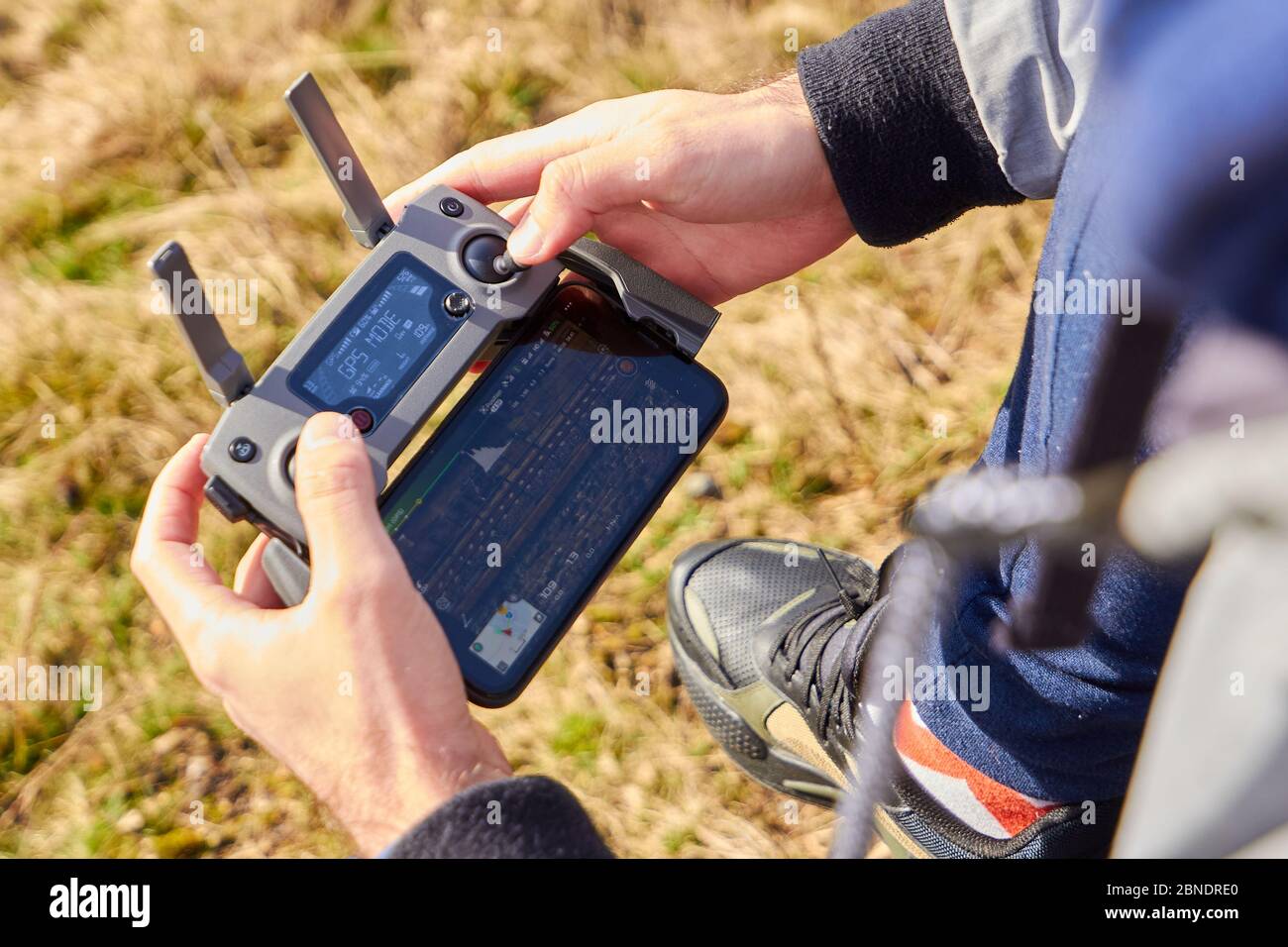 Close up mans hands holding drone remote controller with smartphone in the field. Concept of aerial shooting and flying, San Francisco, May 2020. Stock Photo