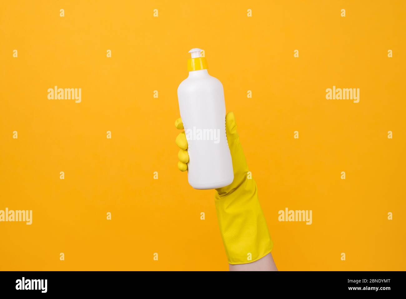 Cropped closeup photo of hand in yellow glove holding a bottle of detergent on yellow background Stock Photo
