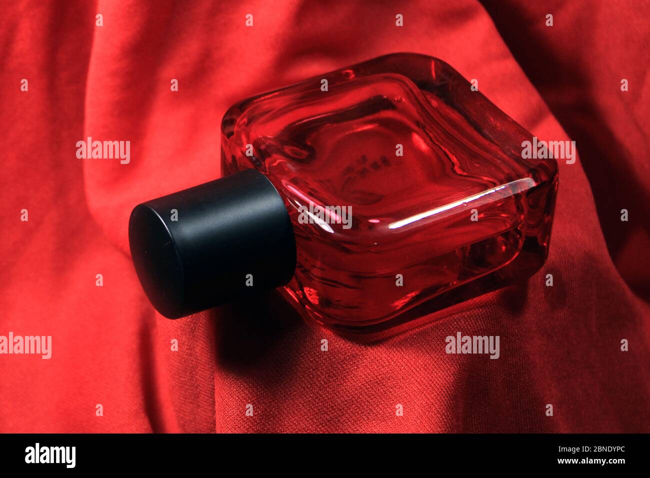 Red color men perfume bottle isolated on red silk background. Red perfume bottle with black cap