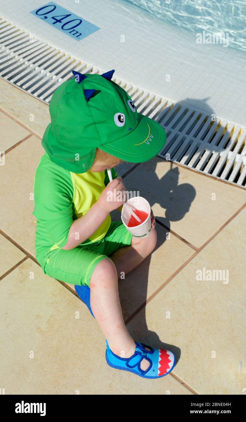A small child takes a break from playing in the pool to enjoy a refreshing cold drink Stock Photo
