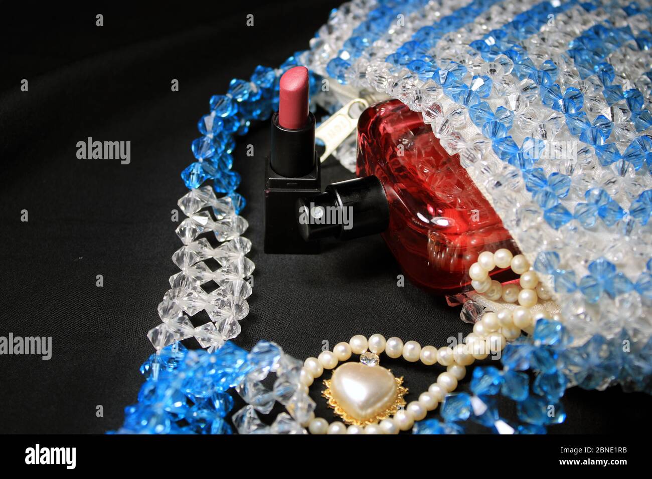 Red perfume bottle, natural spray. Red color men perfume bottle isolated on colorful plastic bag with female accessories. Stock Photo