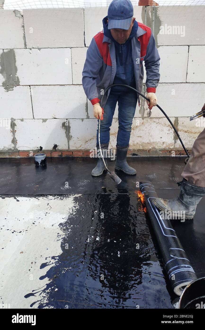 A waterproofing specialist with an assistant melts the bituminous resin  with a blowtorch and seals a reliable roll material. Hermetic covering of  roof Stock Photo - Alamy