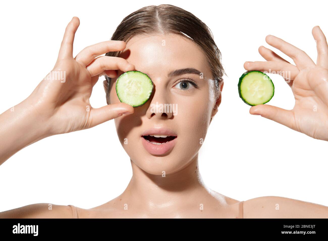 Portrait of beautiful young woman with fresh cucumber on face over white background. Concept of cosmetics, makeup, natural and eco treatment, skin care. Shiny and healthy skin, fashion, healthcare. Stock Photo