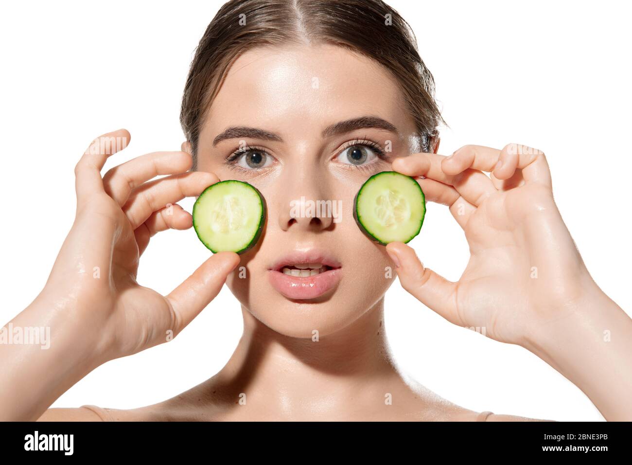 Portrait of beautiful young woman with fresh cucumber on face over white background. Concept of cosmetics, makeup, natural and eco treatment, skin care. Shiny and healthy skin, fashion, healthcare. Stock Photo