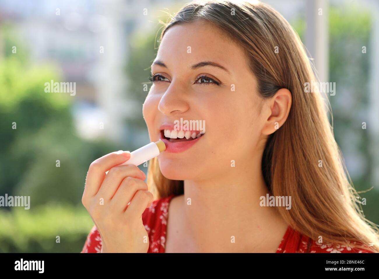 Smiling young woman applying sun protection on her lip outdoor Stock Photo