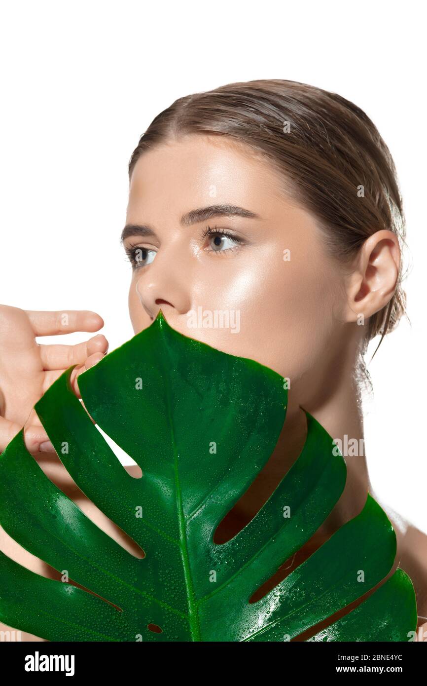 Close up of beautiful young woman with green leaves on her face over ...
