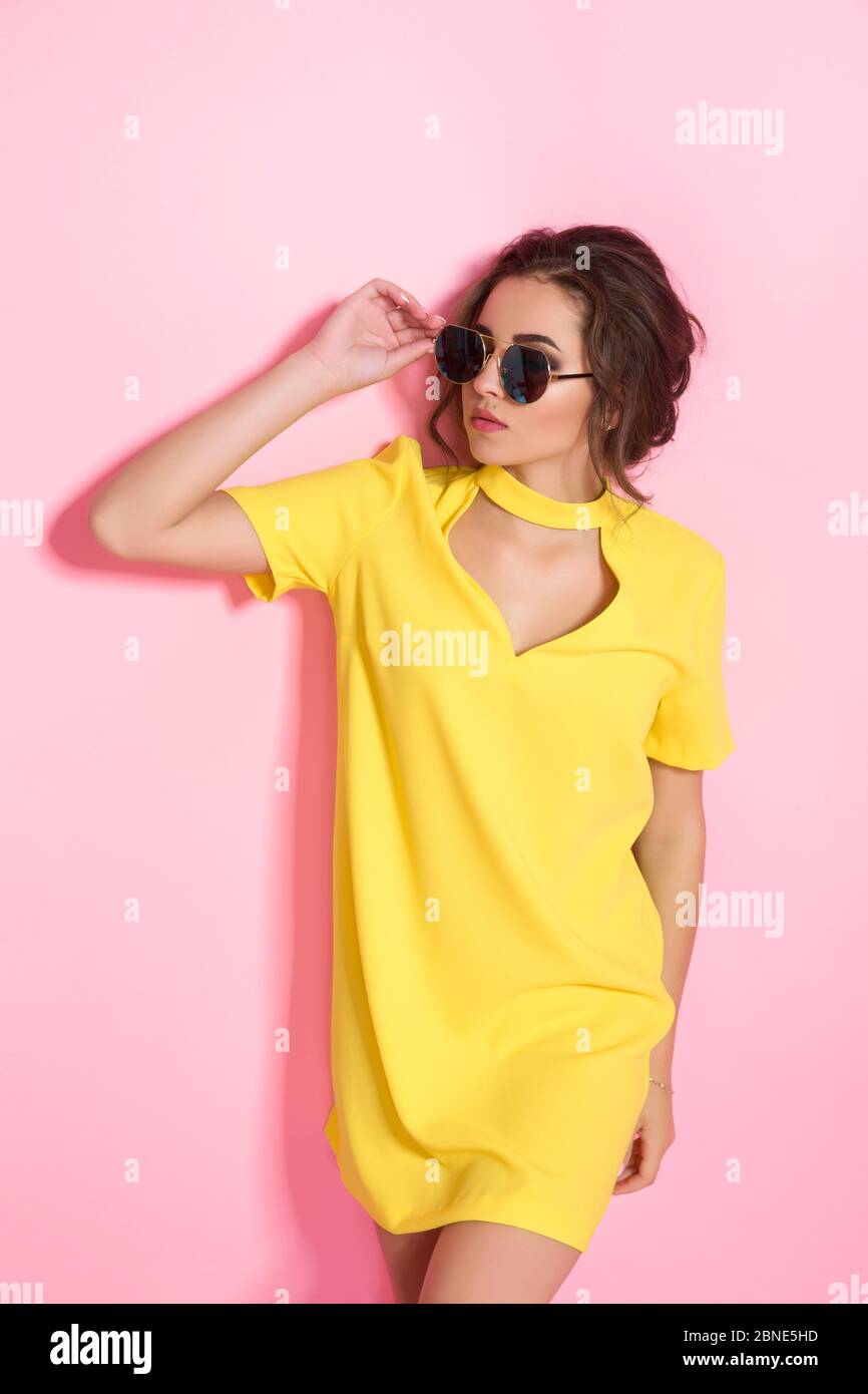 Beautiful girl wearing yellow dress and sunglasses posing on pink ...