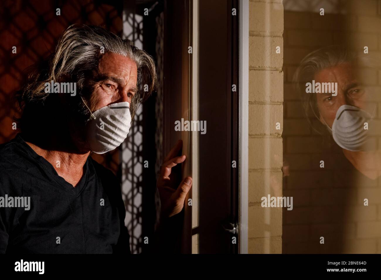 coronavirus crying male medical mask quarantine self isolation concept, depressed distraught mans reflection in window with tears wearing medical mask Stock Photo