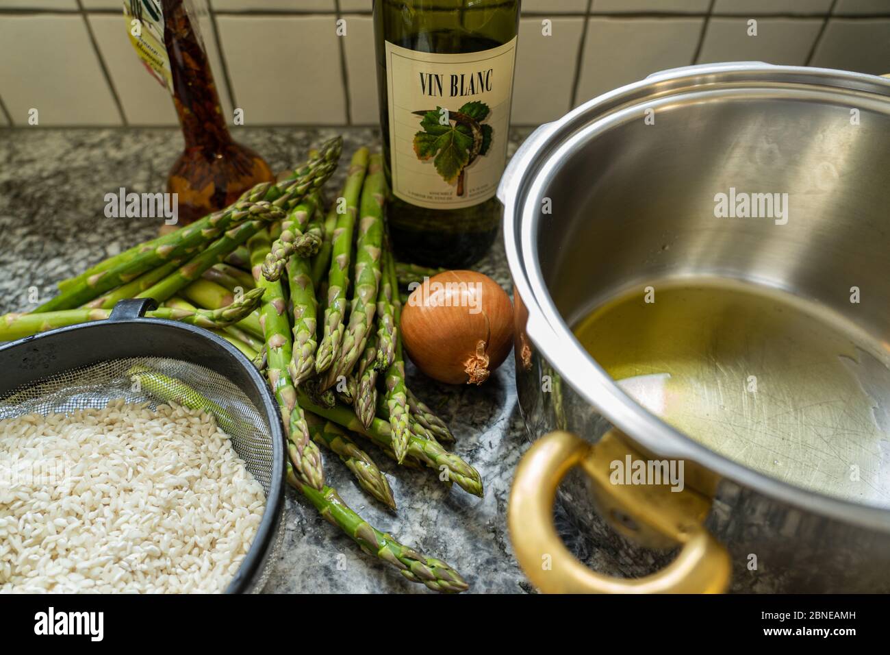 Cooking some Risotto rice with asparagus, onion and white wine. Pan with olive oil on granite background. High angle view. Stock Photo