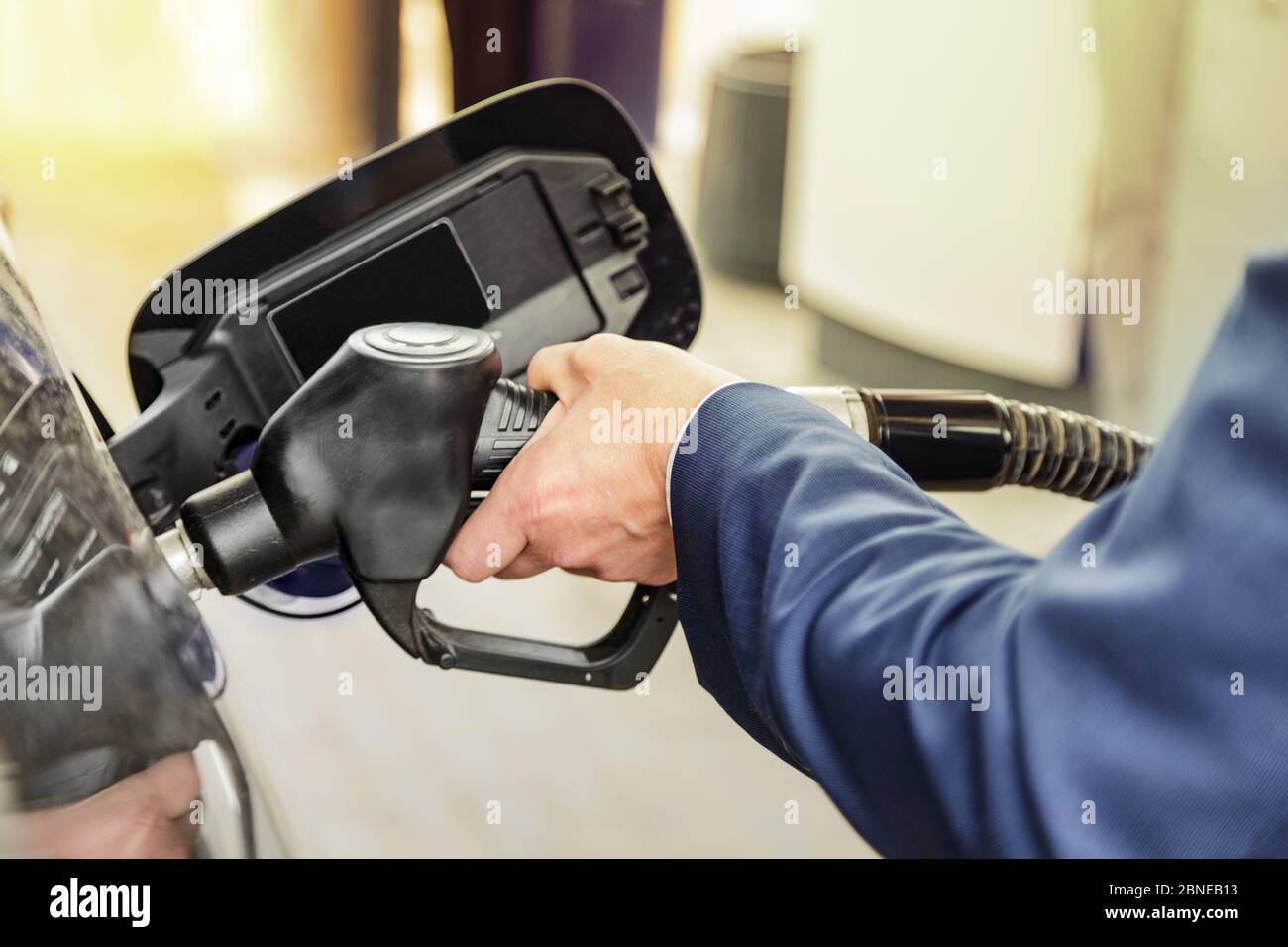 Businessman refuel his car. Close up of a mans hand in blue suit refilling the car with a gas pump. Stock Photo