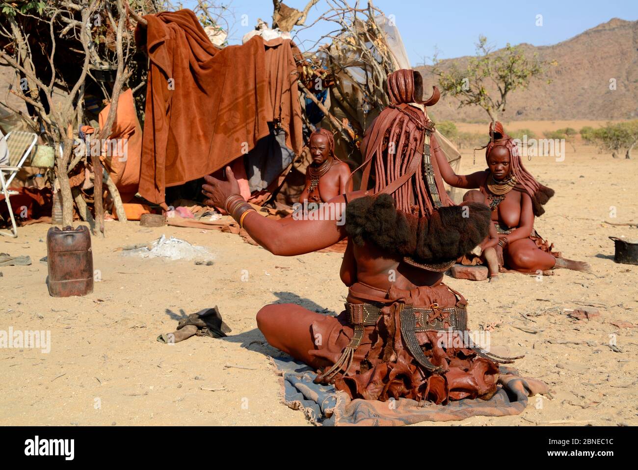 Himba woman greeting and talking to her neighbours in the morning at temporary village in the dry season, Marienfluss Valley, Kaokoland Desert, Namibi Stock Photo