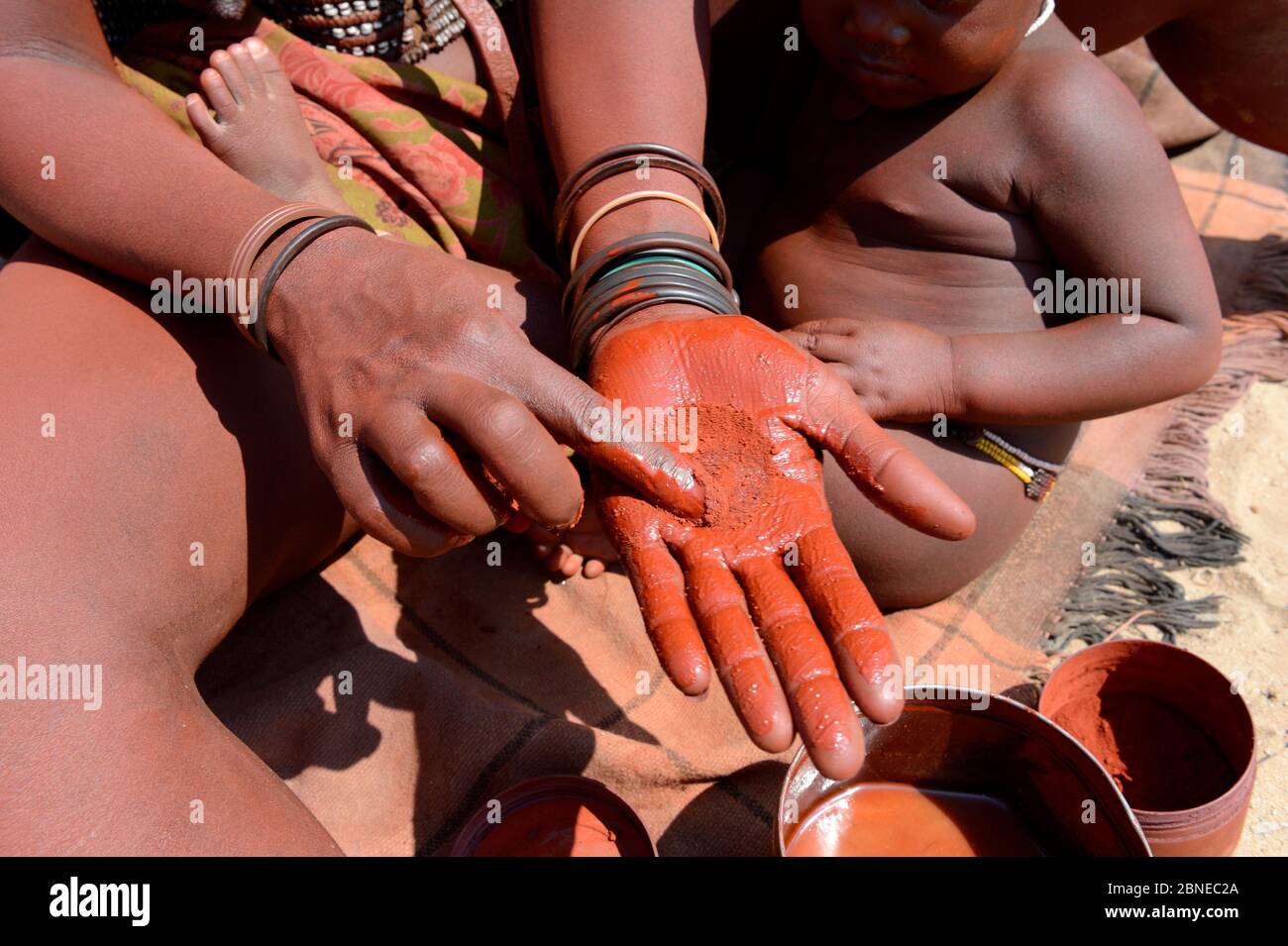 Himba woman mixing ochre with butter to make Otjize, Marienfluss Valley. Kaokoland, Namibia. October 2015 Stock Photo
