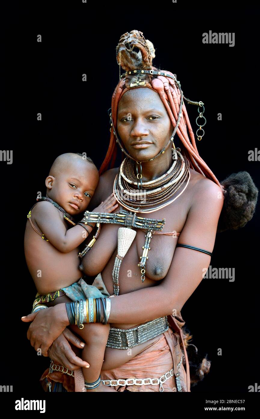 Himba woman with traditional hair and jewellery, holding her her baby, Kaokoland, Namibia October 2015 Stock Photo