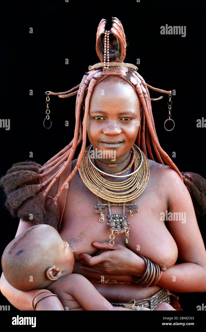 Himba woman with traditional hair and jewellery, nursing her baby. Kaokoland, Namibia October 2015 Stock Photo