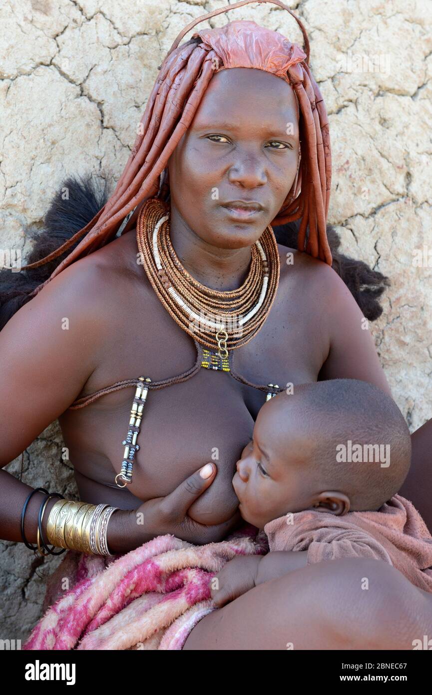 Himba woman with the typical ornaments nursing her baby. Kaokoland, Namibia October 2015 Stock Photo