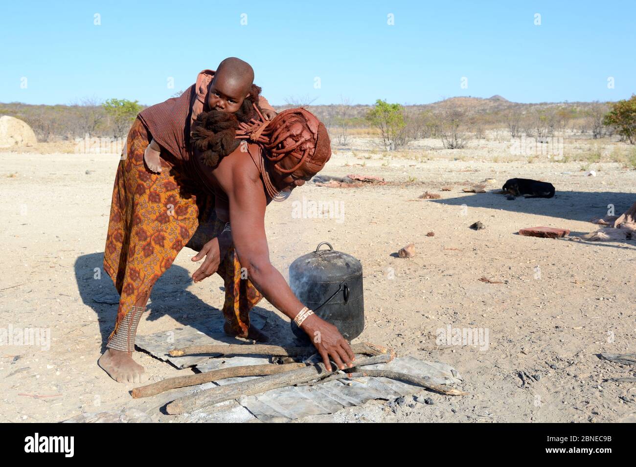 Himba woman with baby preparing the fireplace, Etanga, Kaokoland Desert, Namibia. October 2015 Stock Photo