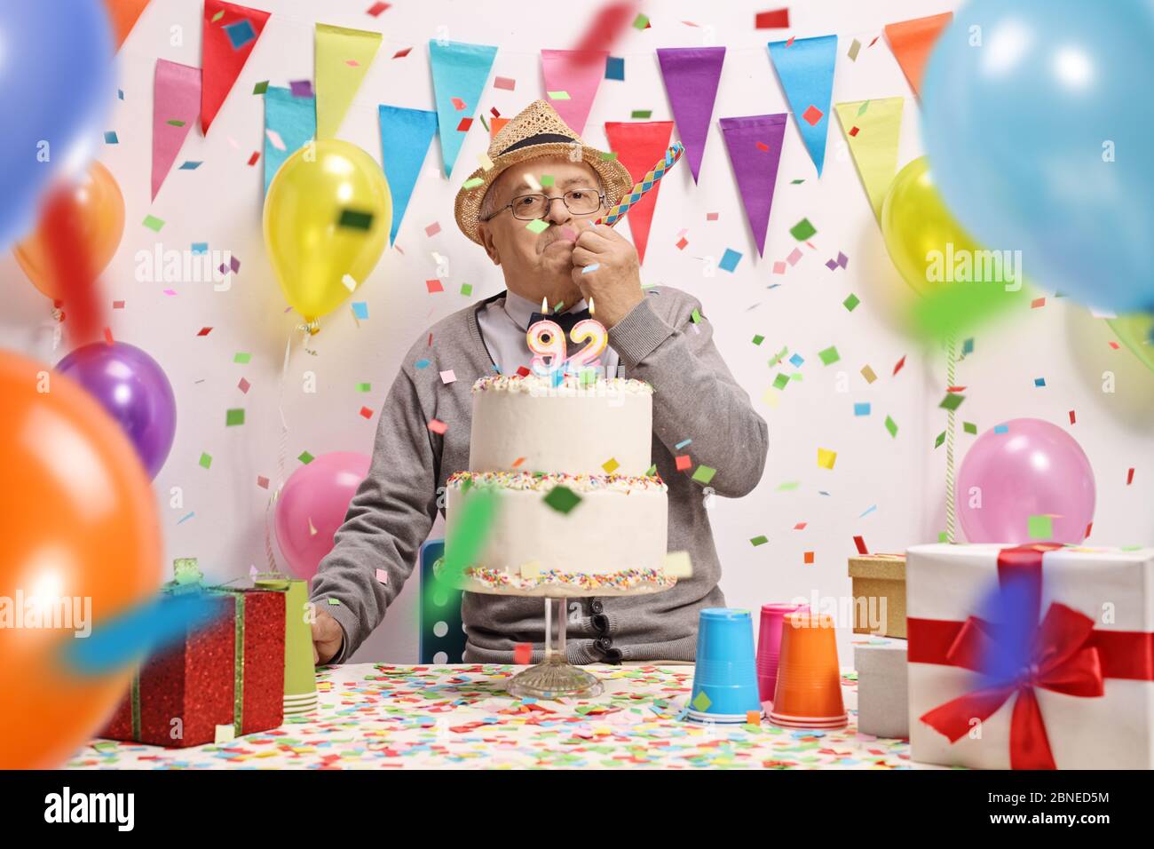 Elderly man celebrating birthday with a cake, balloons and confetti Stock Photo