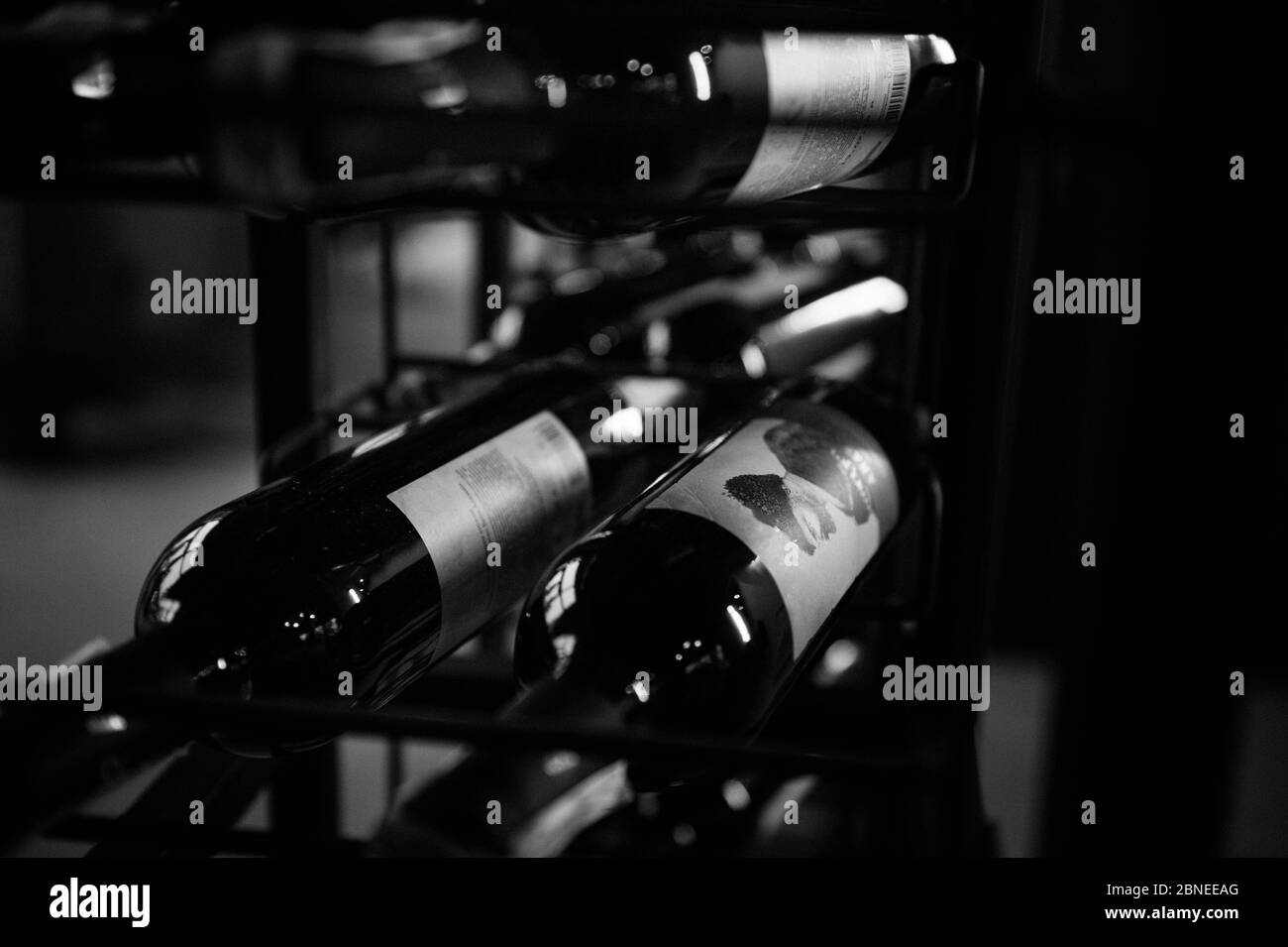 Red wine bottles stacked on wooden racks shot with limited depth of field. Black and white photo. BW photo Stock Photo
