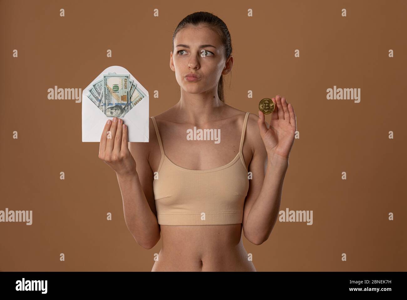 https://c8.alamy.com/comp/2BNEK7H/discomposed-pretty-brunette-girl-with-natural-makeup-dressed-in-beige-bra-holds-white-envelope-in-one-hand-and-bitcoin-golden-coin-in-other-2BNEK7H.jpg