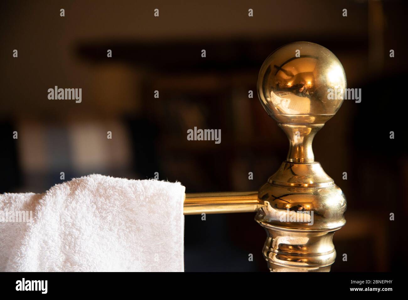 Generic image of the concept of a hotel stay - white cotton towel on old brass bedhead with traditional knob in a quaint hotel bedroom in The Cotswold Stock Photo