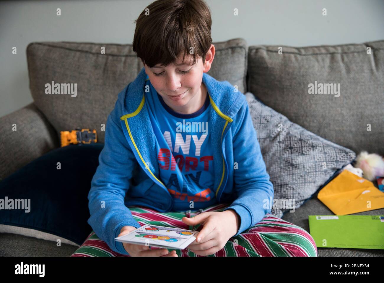 Smirking Teen Boy Reads birthday Card While Sitting on Couch in Pjs Stock Photo