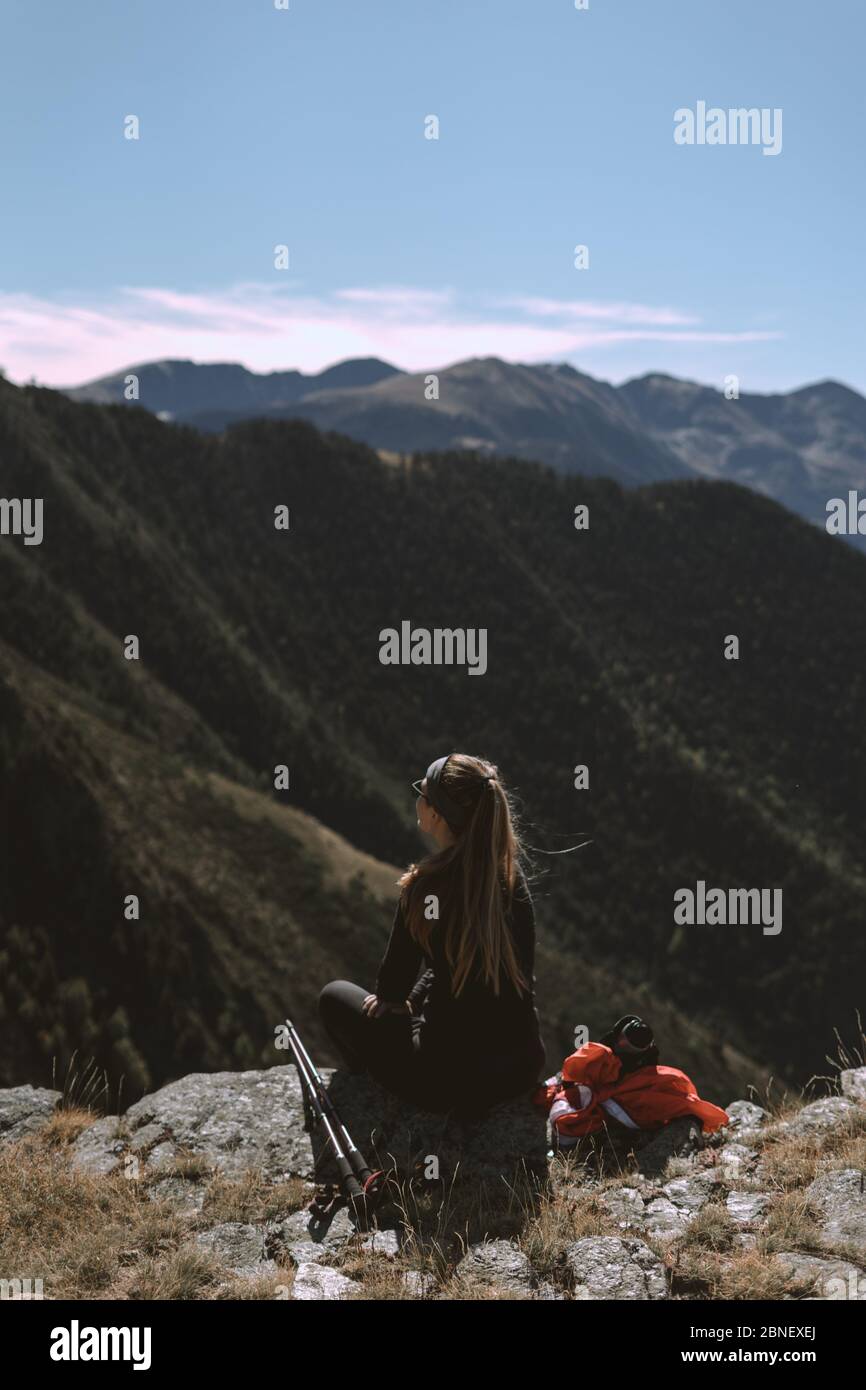 Girl in the mountains watching the landscape next to her mountain sticks and her backpack to climb to the top Stock Photo