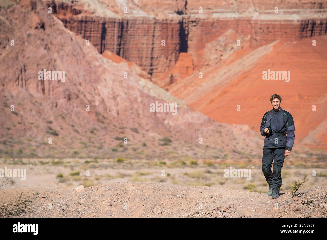 Man in motorcycle gear, standing in front of red sandstone formations Stock Photo