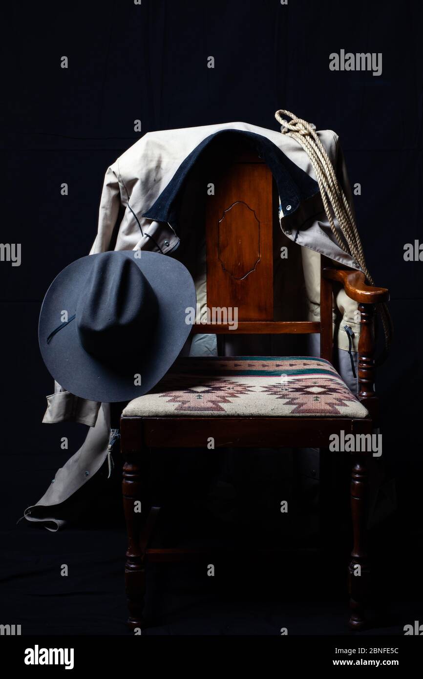 Cowboy hat, duster, rope and a chair with a black background, vertical Stock Photo