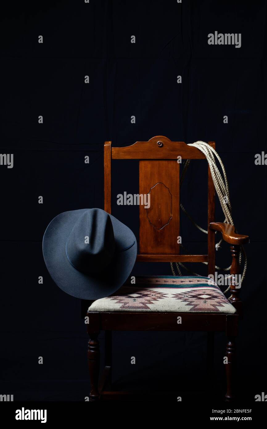 Gray cowboy hat, cattle rope and a chair with a black background, vertical Stock Photo