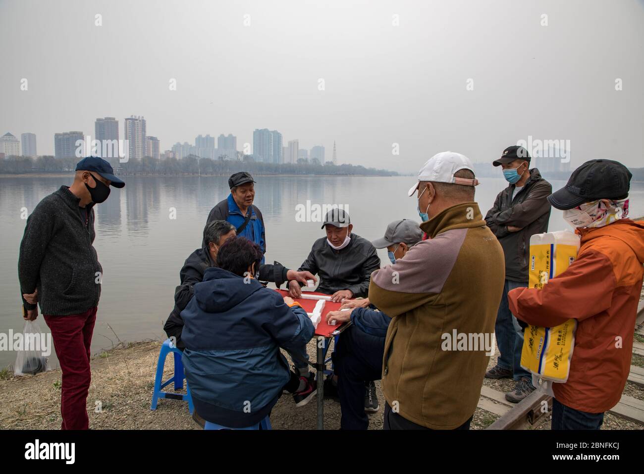 Citizens surround four old men who play Mahjong, a Chinese traditional tile-based game, at the embankment of Songhua River, Jilin city, northeast Chin Stock Photo